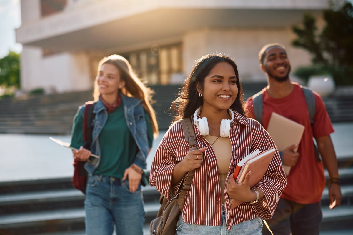 Happy student going on a lecture at the university with friends in the background
